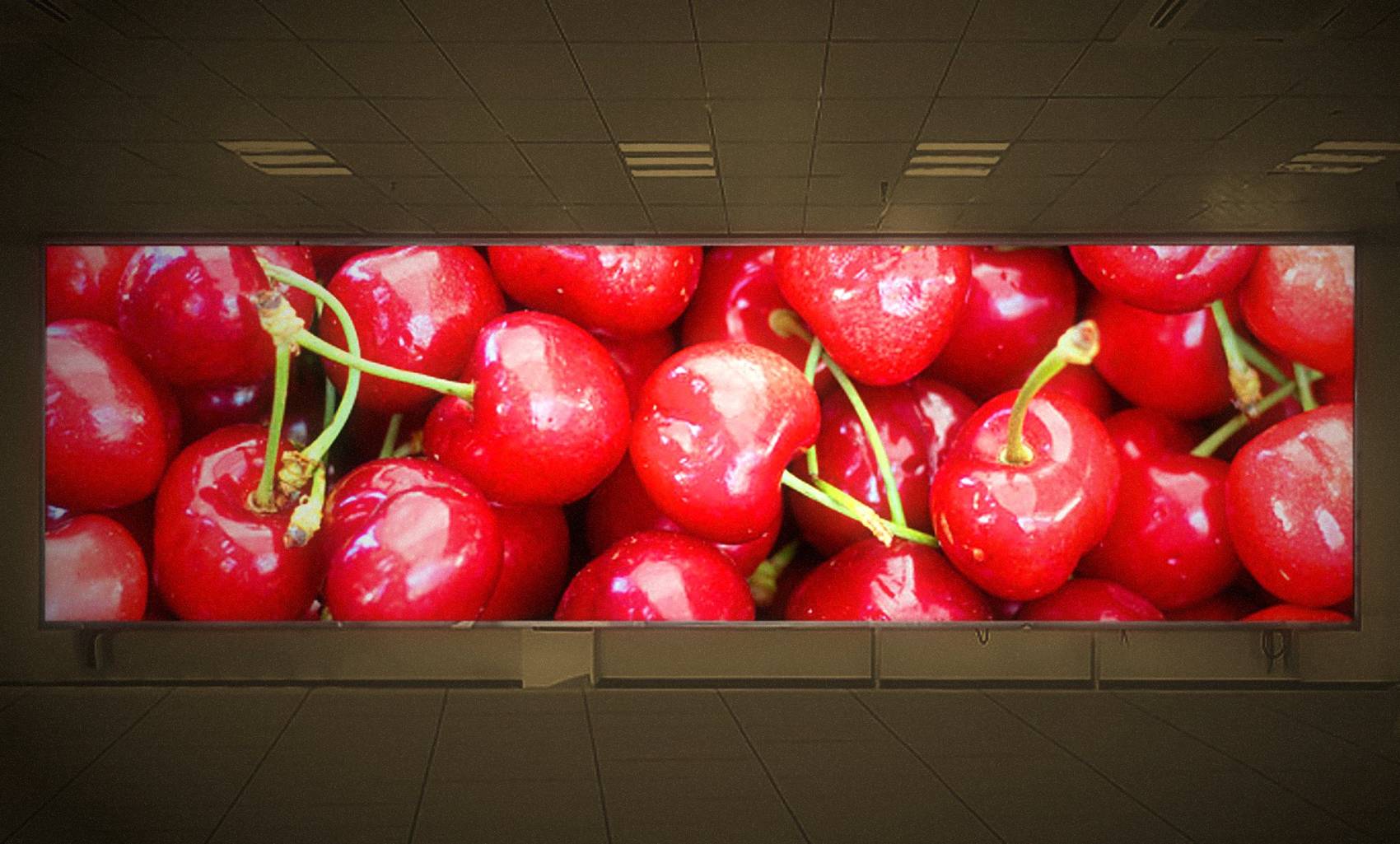 A wide modular LED display filling a lobby wall with a close-up of red cherries